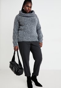 Suéter gris de gran tamaño con cuello de cisne, combinado con pantalones gris oscuro. Un bolso negro y botas de tobillo completan el look.