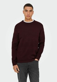 Bordeaux gebreide trui met een textuurpatroon, geribbelde ronde hals en lange mouwen. Gepaard met donkergrijze broek, minimaal ontwerp.