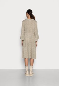 Robe midi à motif floral en beige clair, avec des manches cloche et une taille cintrée. Associée à des bottines brunes.