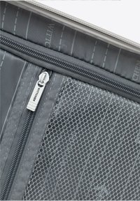 Bolsa gris con cremallera y bolsillo de malla, con una superficie texturizada y un tirador de cremallera plateado con el nombre de la marca. El forro interior tiene rayas verticales.