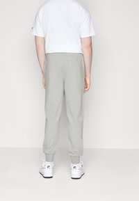 Grå bomullsjoggers med elastisk midjeband, avsmalnande ärmslut och avslappnad passform, kombinerat med vita sneakers. Bakvy visas.