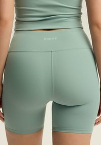 Jasnozielone, elastyczne szorty sportowe z wysokim stanem i małym logo z tyłu, o gładkiej, matowej fakturze.