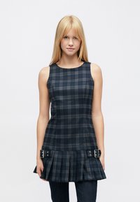 Marineblau kariertes ärmelloses Oberteil mit plissiertem Saum und silbernen Hardware-Akzenten an der Taille. Glatter Stoff mit strukturierter Passform.