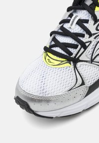 Scarpa da corsa bianca in rete con lacci neri, dettagli riflettenti silver e suola in gomma nera. Presenta un dettaglio giallo vicino ai lacci.