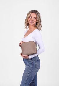 Béžová syntetická kabelka s zaobleným tvarem, texturovaným povrchem a zipem. Jednoduchý detail loga na přední straně, umístěný na boku.