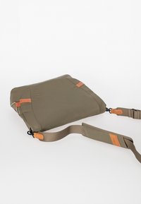 Borsa a tracolla verde oliva realizzata in materiale resistente, con dettagli in pelle marrone a contrasto e tracolla rimovibile dalla lunghezza regolabile.