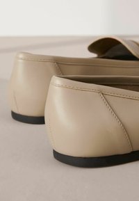 Ballerine in pelle beige con punta arrotondata e suola bassa in gomma nera. Presentano cuciture visibili e una superficie liscia.