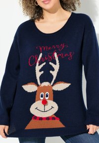 Marinblå stickad tröja med ett renmotiv med röd nos och dekorativ krage. "God Jul" text i rött ovanför motivet.