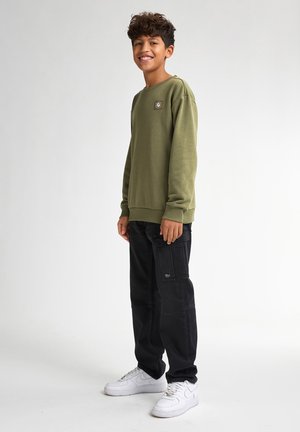Olijfgroene sweatshirt met ribgebreide manchetten en onderrand, met een klein logopatch. Gecombineerd met zwarte cargobroeken en witte sneakers.