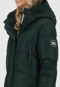 Giacca imbottita verde con cappuccio, chiusura a zip, tasche laterali e patch con logo sulla manica. Tessuto morbido e liscio con dettagli di cucitura.