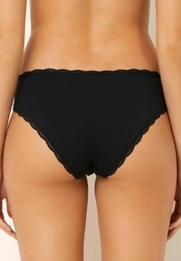 Zwarte katoenen slip met geschulpte kantafwerking. Heeft een gladde, aansluitende pasvorm en een lage taille. Geen aanvullende patronen of onderdelen zichtbaar.