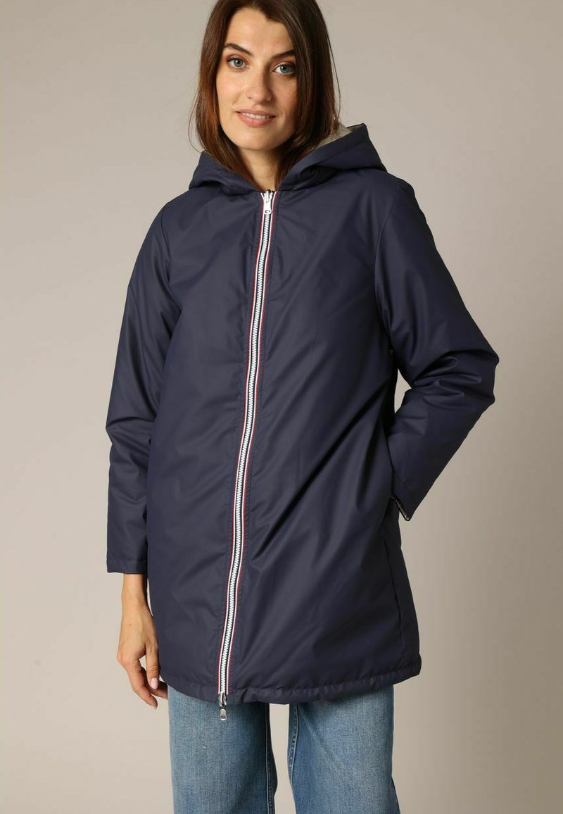 Veste imperméable bleu marine avec capuche, dotée d'une fermeture éclair à l'avant avec accents rouges et blancs, et d'une coupe décontractée avec des manches longues.