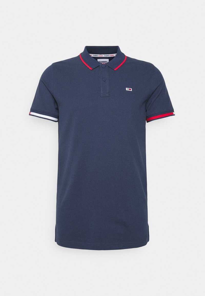 Polo bleu marine en coton, avec un col rouge, des accents rayés rouges et blancs sur les manches, et un petit logo sur la poitrine.