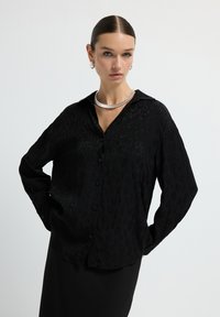 Black button-up shirt with subtle tonal leopard print design, long sleeves, and a relaxed fit, paired with a sleek black skirt.
