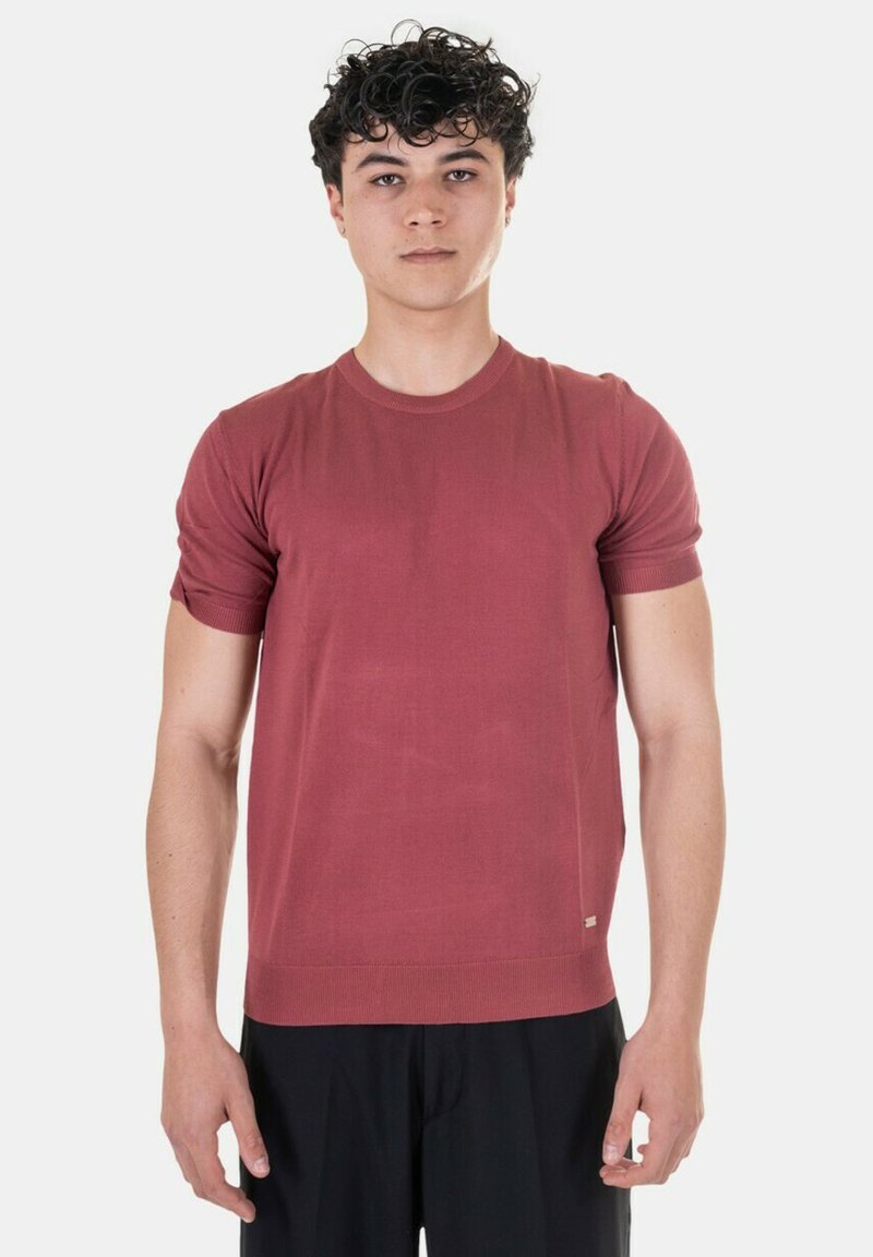 T-shirt rosso a maniche corte in maglia con collo rotondo e polsini a costine. Texture morbida, taglio aderente, branding minimale all'orlo.