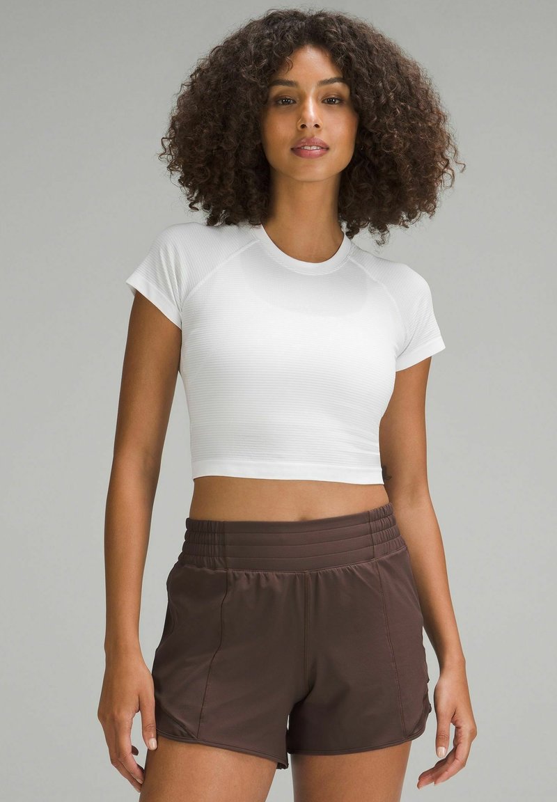 Fehér crop top, bordás textúrával, amelyet magas derekú barna sportnadrággal párosítottak, rugalmas derékkal és oldalsó zsebekkel.