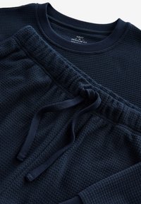 Marineblå langærmet top i vaffelstrik med matchende bukser med elastisk talje og snøre, vist liggende fladt.