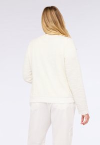 Cremefarvet jakke med afslappet pasform, der har et glat, let stof og en simpel, uforet design. Lange ærmer og hojlængde.