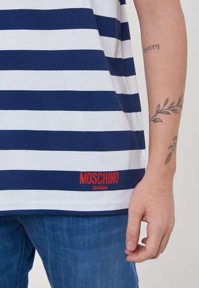 T-shirt a righe blu navy e bianche con vestibilità rilassata, caratterizzata da un logo rosso "MOSCHINO SWIM" nella parte inferiore e un tessuto testurizzato.