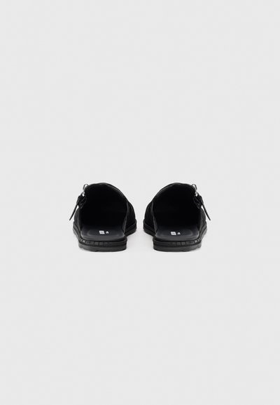 Black slip-on shoes with a smooth interior and textured outer fabric. Rounded toes, flat soles, and minimalist design. No visible branding.