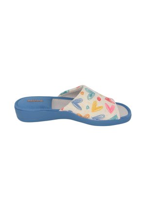 Zapatilla con suela azul y parte superior de tela color crema que presenta patrones de corazones y espirales coloridos, puntera abierta y diseño sin cuello.