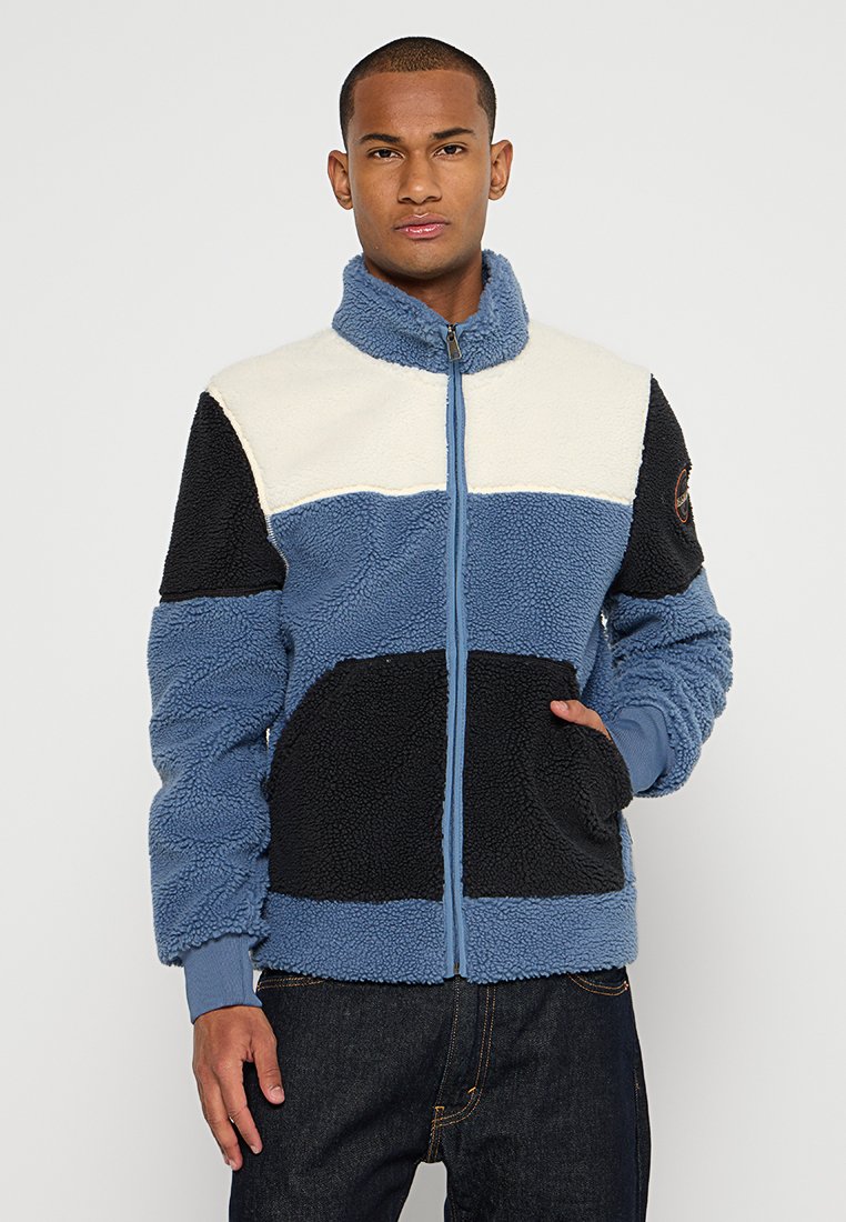 Chaqueta de forro polar con cremallera frontal, con paneles en azul, crema y negro. Tejido texturizado, dos bolsillos laterales y puños acanalados.