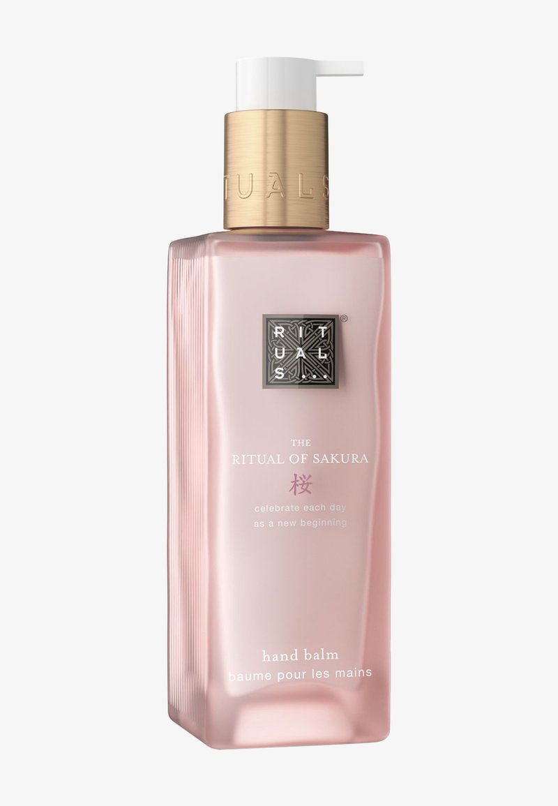 Roze rechthoekige fles van Rituals The Ritual of Sakura handbalsem met witte pomp en gouden kraag, gelabeld in het Engels en Frans.