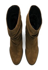 Botas de tobillo de ante marrón con un diseño arrugado, punteras redondeadas y forro interior negro. Las suelas son planas y ligeramente texturizadas.