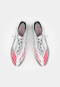 Ghete de fotbal albe cu accente în bandă roșie și neagră, având un design elegant, textură minimală și șireturi și branturi vizibile.