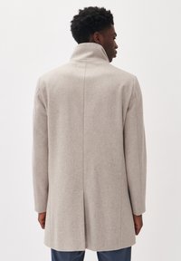 Abrigo de lana gris claro con cuello alto, corte recto, hombros caídos y una ventileta en la parte posterior central. Textura suave y detalles mínimos.