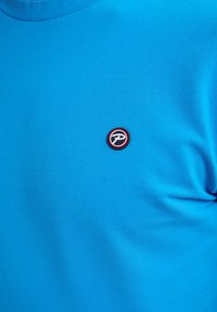 T-shirt in cotone blu con scollatura rotonda e un logo circolare rosso e nero sul petto, texture liscia e vestibilità classica.