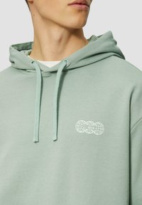 Felpa verde chiaro realizzata in morbido tessuto, con tasca frontale e grafica di un globo bianco sul petto. Coulisse sul cappuccio.