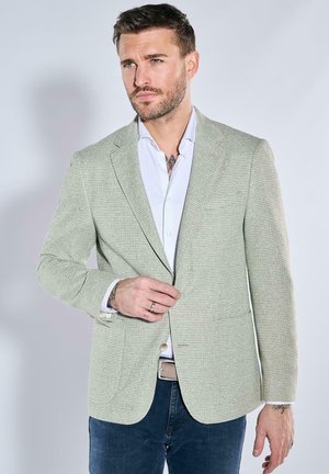 Light green textured blazer with a notched lapel, single button closure, and two front pockets, worn over a white shirt and blue jeans.