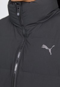 Schwarze gepolsterte Jacke mit hohem Kragen, ausgestattet mit einem durchgehenden Reißverschluss und einem dezenten grauen Puma-Logo auf der linken Brust. Weicher, texturierter Stoff.