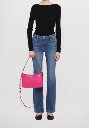 Różowa torebka z teksturą na ramię, trzymana w dłoni. Czarna bluzka z długim rękawem, niebieskie rozszerzane jeansy i czarne baleriny dopełniają strój.