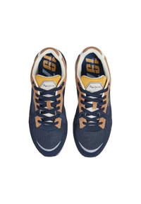 Sneaker blu navy con accenti in suede marrone, parte superiore in mesh strutturato, suola bianca e soletta gialla a contrasto con logo e elementi di design audaci.