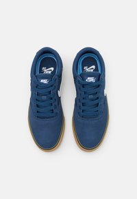 Baskets en daim bleu marine avec un bout rond, un laçage et un logo Nike blanc. La semelle en caoutchouc présente une semelle extérieure marron clair.