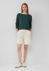 Haut à manches longues texturé vert associé à un short crème. Le short possède une taille à cordon et des poches latérales. Des baskets blanches complètent la tenue.