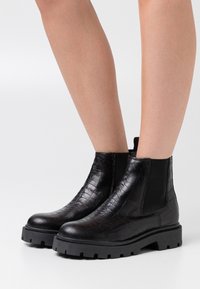 Bottines en cuir noir avec une texture crocodile, panneaux latéraux élastiques, semelle en caoutchouc épaisse et design à bout rond.