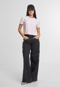 Lyse rosa avskåret t-skjorte med hvit kant, sammen med løse, svarte denim cargo-bukser med sidelommer og frynsete hem. Svart caps brukt.