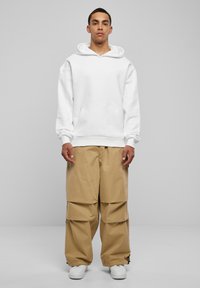 Felpa bianca con tasca a marsupio, abbinata a pantaloni cargo oversize color beige, con cordino all'orlo. Sneakers bianche completano l'outfit.