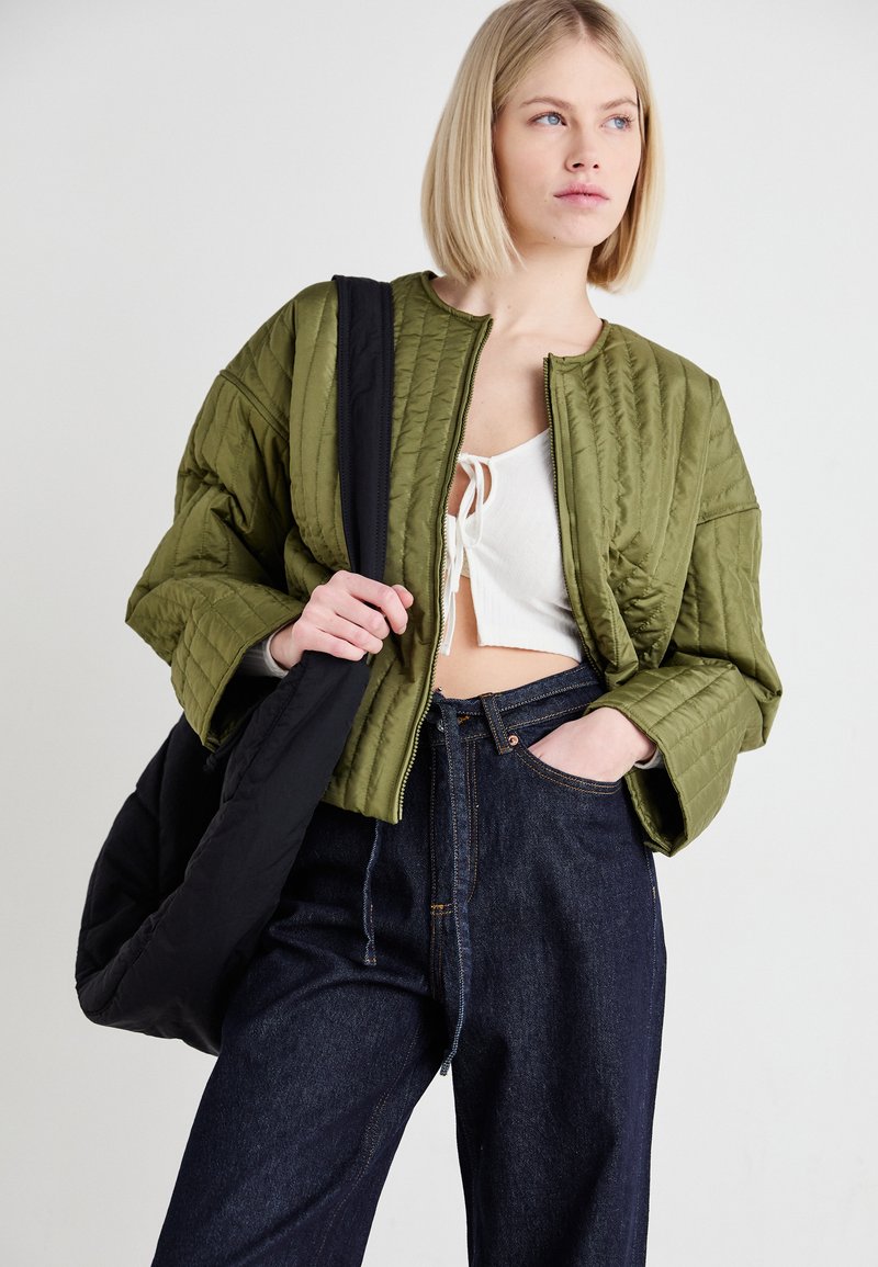 Veste bomber matelassée vert olive avec des bretelles noires, col rond et coupe cropped, associée à un jean en denim noir taille haute.