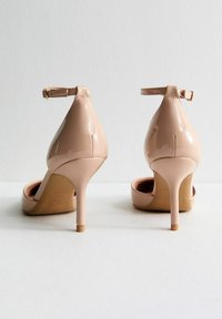 Naakt patentleren hoge hakken met een spitse neus en enkelbandje, met een stilettotoeve en een gladde, glanzende textuur.