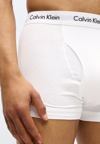 White cotton boxer briefs with Calvin Klein logo in black on the waistband. Fitted design with smooth texture and side opening detail.