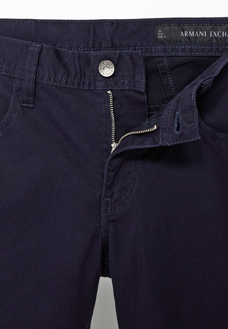 Granatowe, slim fit dżinsy Armani Exchange z częściowo rozpiętym zamkiem i zapiętym paskiem, rozmiar 31, widoczna metka marki wewnątrz.