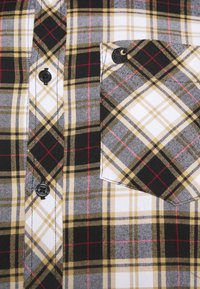Camicia a maniche lunghe a quadri con motivi check in nero, bianco, giallo e rosso. La tasca anteriore presenta anch'essa un design a quadri simile.