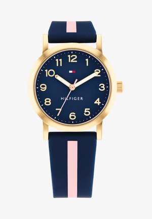 Relógio com bracelete de silicone azul-marinho, caixa banhada a ouro, marcadores de hora brancos e destaque em rosa. Apresenta um mostrador azul e um logotipo na parte superior.