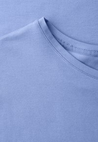 Tissu en coton bleu clair à col rond avec coutures visibles et détail de col sans couture, présenté en gros plan.