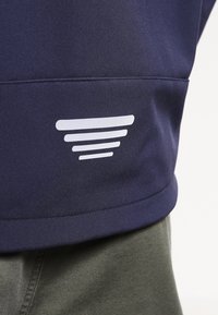 Vêtement bleu marine à la texture lisse, avec un logo blanc composé de cinq lignes horizontales sur le côté inférieur. Gros plan sur le matériau.