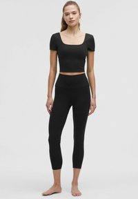 Crni krojeni top s kratkim rukavima i kvadratnim izrezom, u kombinaciji s crnim leggingama visokog struka, oboje izrađeno od rastezljivog materijala.
